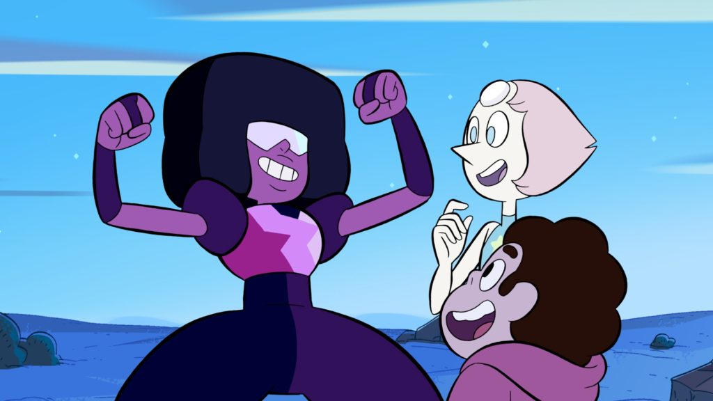 (Zeichentrick) Garnet, eine rot-rosa-schwarze Figur aus Steven Universe, reckt triumphierend die Arme in die Höhe. Ihre Freund*innen Pearl und Steven freuen sich mit ihr.