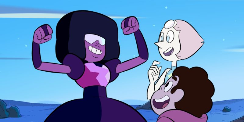 (Zeichentrick) Garnet, eine rot-rosa-schwarze Figur aus Steven Universe, reckt triumphierend die Arme in die Höhe. Ihre Freund*innen Pearl und Steven freuen sich mit ihr.